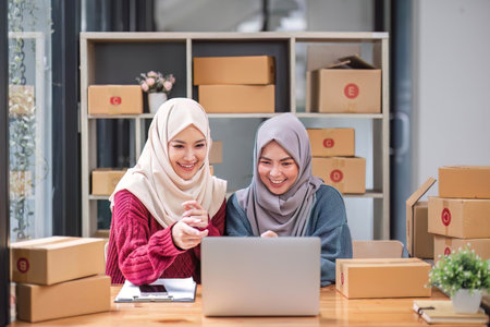 Friend muslim female two work business sme online shopping working on laptop computer with parcel box on desk at home, SME online business and delivery conceptの写真素材