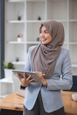 A portrait of a successful Asian Muslim businesswoman stands in her modern office with a digital tablet in her hand.の写真素材