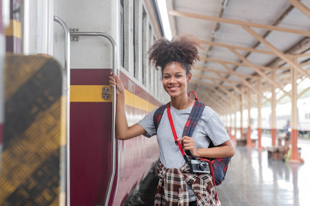 Traveler african asian american woman getting in a train to hop on train, Young woman female standing on train door peeking out looking from door, tourist on a train staionの写真素材
