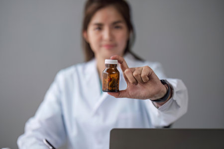 Young beautiful asian woman doctor holding pills bottle writing on document at clinicの写真素材
