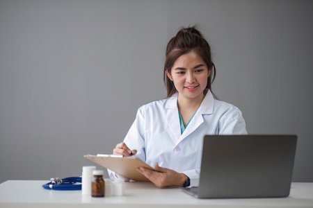 A confident Beautiful, professional female doctor or nurse is working online with a laptop while sitting at a desk in a hospital consultation roomの写真素材