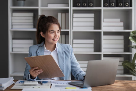 Cheerful business lady working on laptop in office, Asian happy beautiful businesswoman in formal suit work in workplace. Attractive female employee office worker smileの写真素材