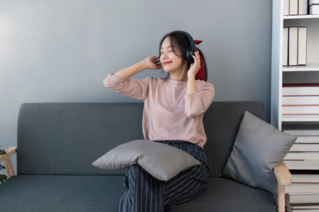 Happy asian woman listening to music from mobile phone while sitting on the the sofa at homes, Smiling girl relaxing with headphones in morning, Time to relax.の写真素材