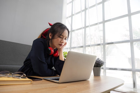 Confused student e-learning with laptop and headphones sitting on a couch in the living room at homeの写真素材