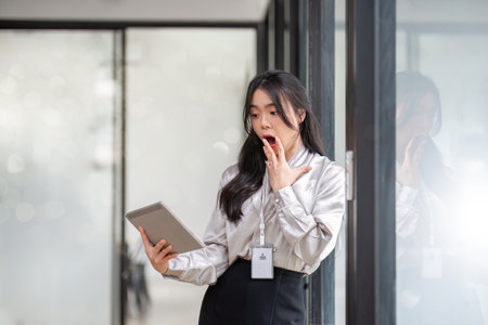 A beautiful and cheerful Asian businesswoman or female boss is showing her clenched fist and looking at her tablet with an excited face, receiving good news and achieving goalsの写真素材