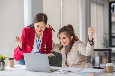 Two Asian businesswoman showing excited expression in front of laptop due to successful results.の写真素材
