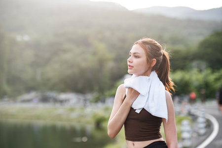 Portrait Young beautiful Asian woman wiping sweat after evening jogging in the park.