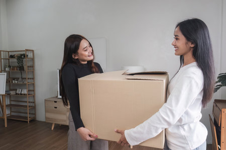 Two young women are carrying cardboard boxes in their room on the day of the move.の写真素材