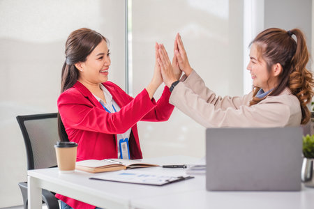 Two Asian businesswoman showing excited expression in front of laptop due to successful results.