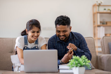 Happy couple using credit card to make online purchases on laptop in living room.の写真素材