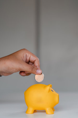 Close up woman puts coins in a piggy bank with a pile of coins to save money.の写真素材