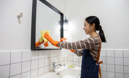 A young maid cleans the bathroom using a cloth and cleaning spray.の写真素材