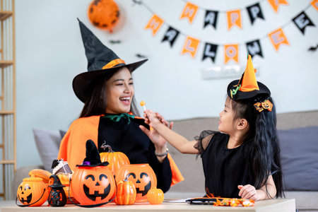 Playful young mother sitting on comfy couch in living room with cute little daughter tells spooky Halloween stories. Funny mom and girl kid have fun at home. Celebration and Autumn holiday conceptの写真素材