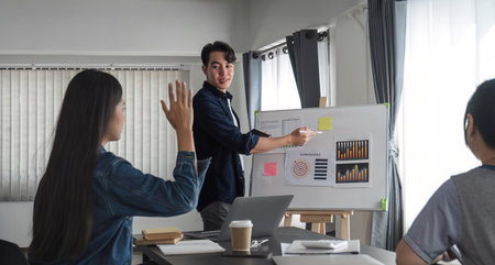 Young businessman explains work plan in meeting to teammates in conference room.