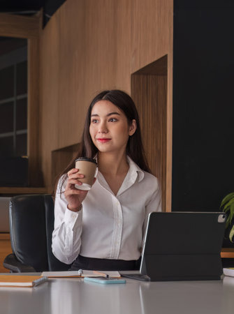 Asian businesswoman drinking coffee with tablet on desk at office.の写真素材