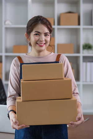 Portrait of Asian young woman SME working with a box at home the workplace.start-up small business...