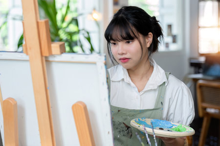 Young female artist works on abstract acrylic painting on canvas in art painting studio.の写真素材