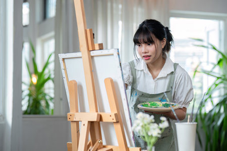 Young female artist works on abstract acrylic painting on canvas in art painting studio.の写真素材