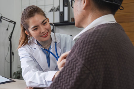 The female doctor in charge holds a stethoscope and listens to the patient. Doctor checking heartbeat examining retired elderly man at home Senior heart disease, health checkup concept health careの写真素材