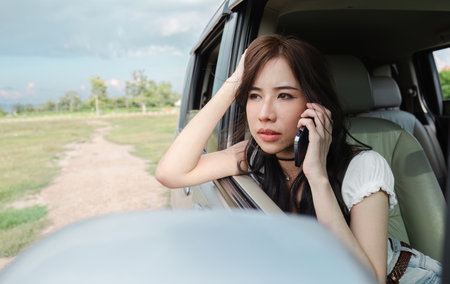 Stressed and confused Asian woman calls insurance on faulty car while traveling togetherの写真素材