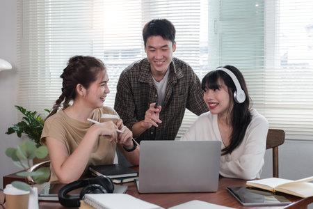A cheerful and intelligent young Asian man is standing and sharing his thoughts in a meeting with his team. University students, friendship, startups, teamworkの写真素材