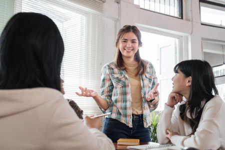 A cheerful and smart young Asian female is standing and sharing her ideas in a meeting with her team. University students, friendship, startups, teamworkの写真素材