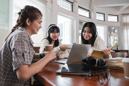 A group of cheerful Asian college students are enjoying talking and discussing their group project while sitting in a coffee shop together.の写真素材
