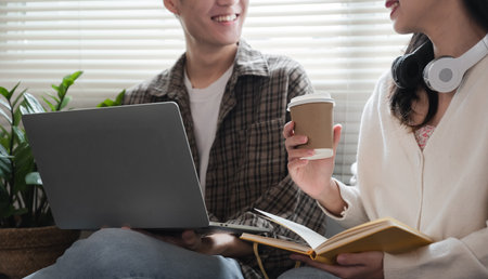 A happy young Asian man and a pretty girl are working on a laptop together, working on a co-project,...