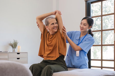 Caucasian senior woman 60s doing physiotherapist with support from nurse. Senior elderly female sitting on sofa in living room workout exercise for patient with caregiver in nursing care.の写真素材