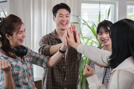 A group of cheerful and happy young Asian friends are gathering together to celebrate the success of a project together in a conference room.の写真素材