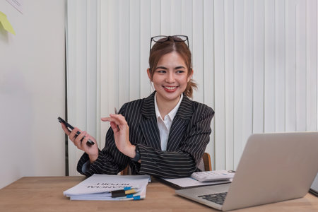 Asian businesswoman in a formal suit in the office is happy and cheerful while using a smartphone to work in her office.の写真素材
