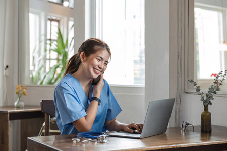 Happy female doctor using laptop to do data work and chat with patients on the phone in office in hospitalの写真素材