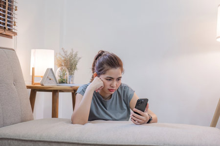 Sad woman reads bad news message Sitting lonely on the sofa in the living room Unhappy woman despairing over loss message on phoneの写真素材