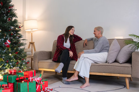 Young woman and mother sitting and talking in living room with Christmas tree and gift boxes. young woman talking Relax on the couch with Mom on Christmas Day or any holiday.の写真素材