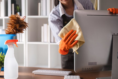 Young woman uses a cleaning cloth to disinfect the computer and equipment on the office table....
