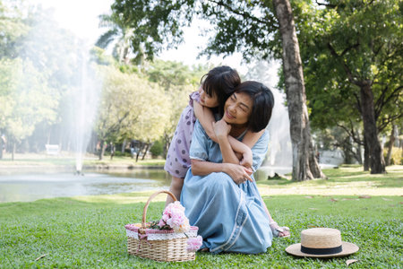 A happy Asian grandparent with her adorable granddaughter while having a picnic in a beautiful park over the weekend together.の写真素材