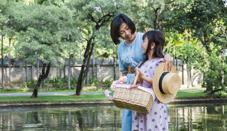 A happy Asian grandparent with her adorable granddaughter while having a picnic in a beautiful park over the weekend together.の写真素材