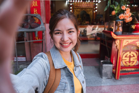 Young female traveler taking pictures at Chinese temple Young Asian woman in blue jacket using...
