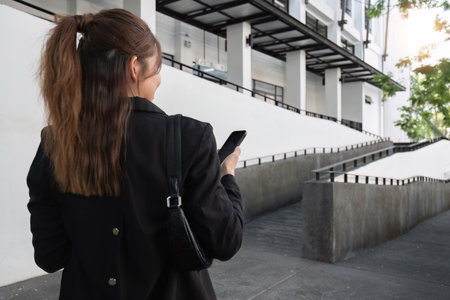 Attractive smiling Asian businesswoman wearing a suit standing in the city using an application on her mobile phone Read news on your smartphone fast connection Check out the outdoor mobile appの写真素材
