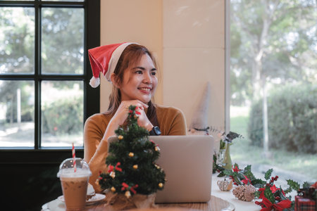 A startup employee writes a report on a laptop on Christmas Eve. In an office decorated with colorful bulbs and lights during the Christmas holidaysの写真素材