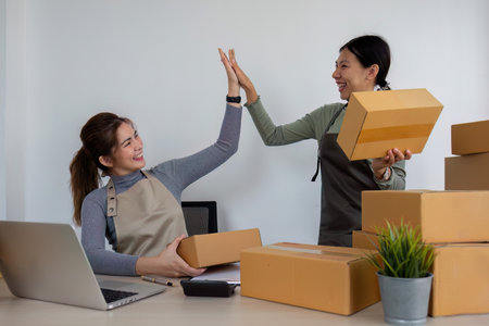 Two Asian entrepreneur women take order and check boxes of products according to customer orders in preparation for delivery.の写真素材