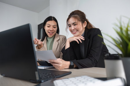 Two Asian businesswomen discuss business planning ideas. Graph analysis on laptop at officeの写真素材