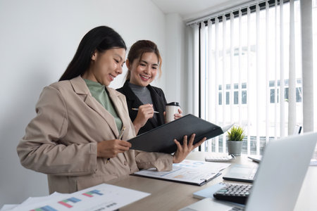 Two Asian businesswomen discuss business planning ideas. Graph analysis on laptop at officeの写真素材