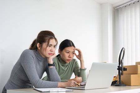Two Asian women selling clothes live on their phones are stressed over problems that arise during the sale.の写真素材
