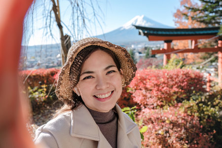 Cheerful Asian female tourist wearing a hat takes a selfie in the background in Japanの写真素材