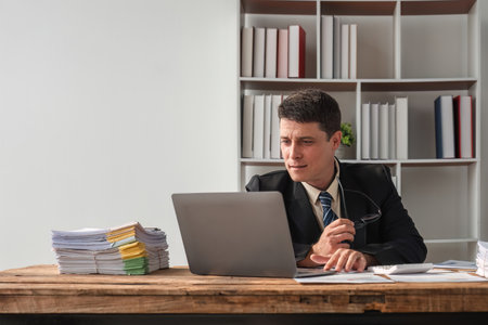 Unhappy young businessman feeling bored and stressed at work looking at laptop with hopeless...