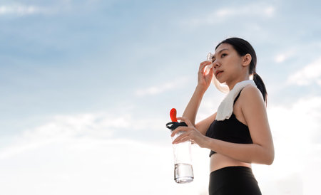 Young Asian woman takes a relaxing walk, wiping off sweat after jogging in the park.の写真素材