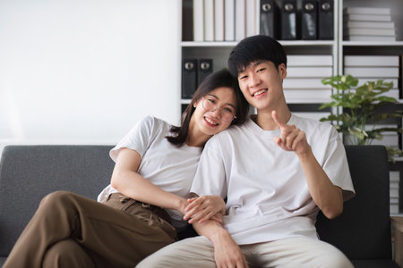 A smiling young couple of boys and girls were sitting on the sofa in the living room, teasing each other with fun.の写真素材
