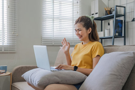 Beautiful Asian woman wearing casual clothes On the sofa using a laptop computer, entertaining with...