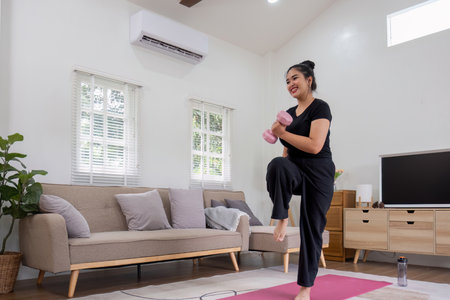 Fat woman exercising at home A beautiful oversized woman in a sports bra and casual pants stands in the living room and exercises.の写真素材